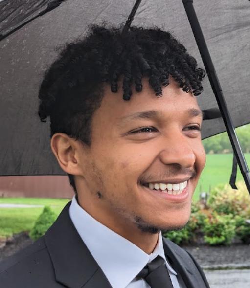 Saleh Hassen smiling in a gray suit while holding an Umbrella.